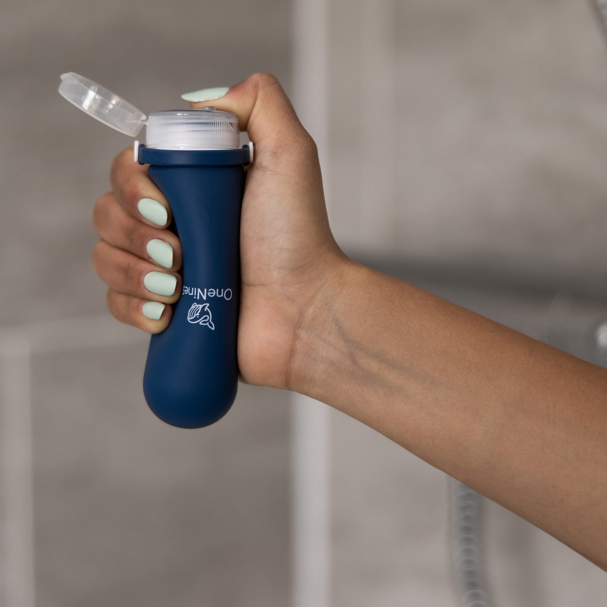 A female squeezing the soft silicone OneNine5 blue bottle in the palm of her hand, with the leakproof cap open.