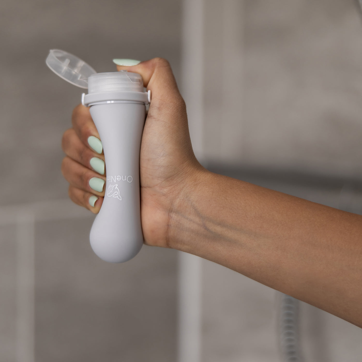 A female squeezing the soft silicone OneNine5 grey bottle in the palm of her hand, with the leakproof cap open.