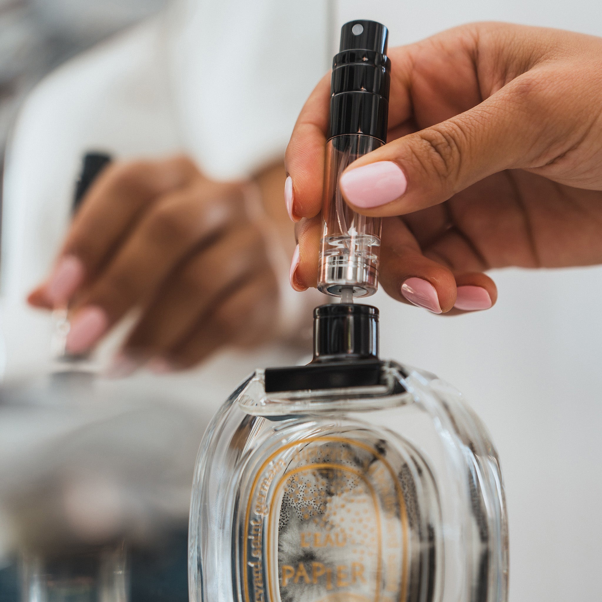 A female refilling the 5ml travel fragrance bottle in a bathroom. Pushing down on the leakproof pump to refill the 5ml travel bottle from a Diptyque 100ml fragrance bottle.