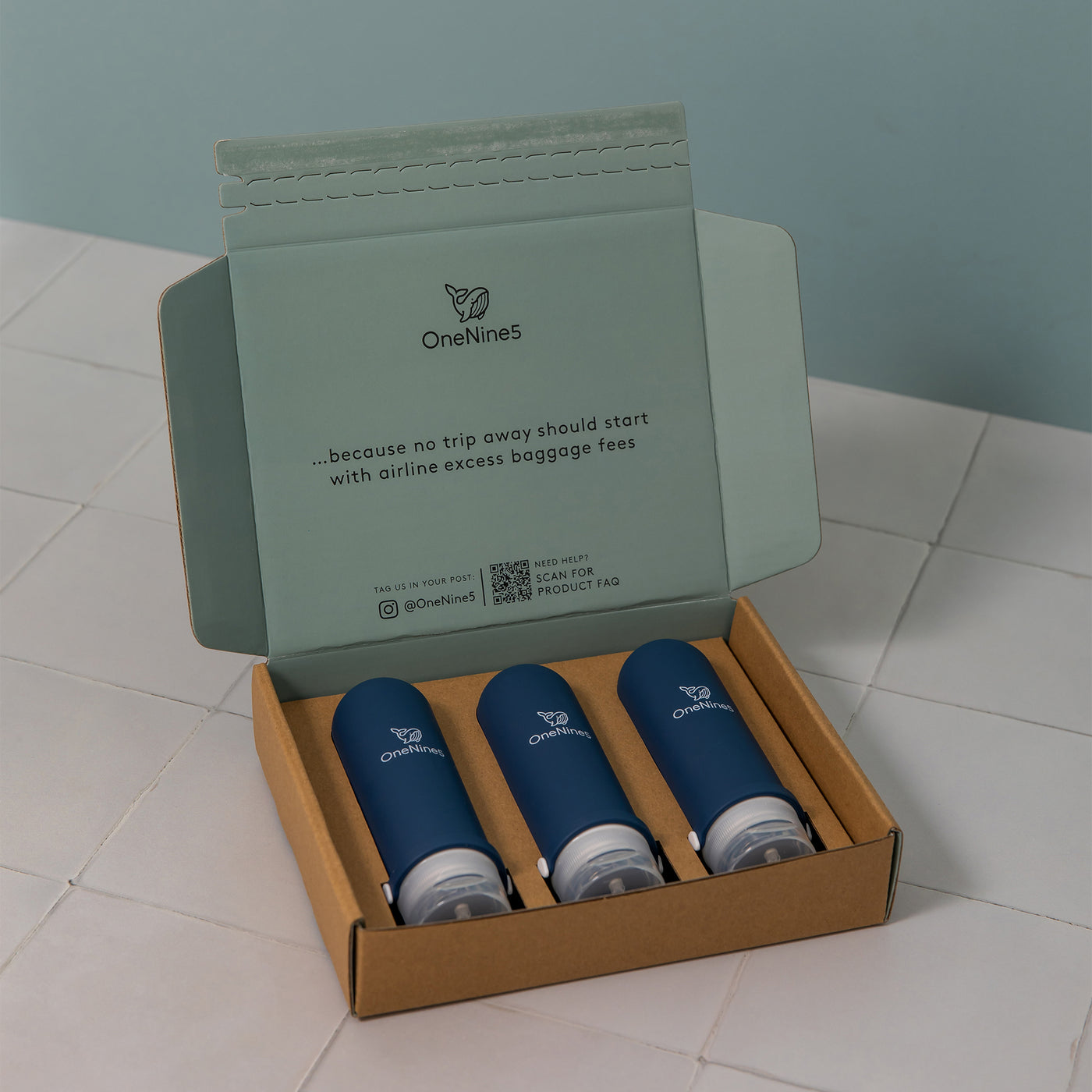 3 pack of blue silicone travel bottles are packed inside a brown, recyclable kraft paper box. Printed inside the packaging is the OneNine5 logo, a QR code and the caption ‘Because no trip away should start with airline excess baggage fees’.