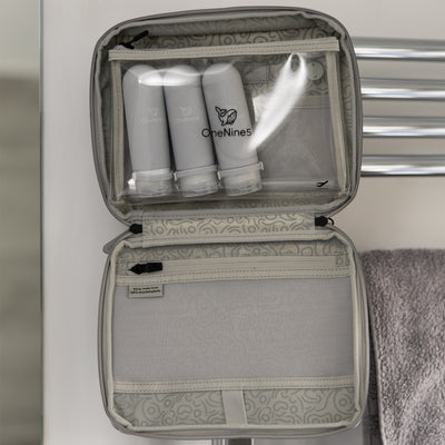 Three grey silicone travel bottles inside the clear toiletry pouch. The pouch is attached inside the OneNine5, Moeraki Grey wash bag, using the hanging hook, in the bathroom.