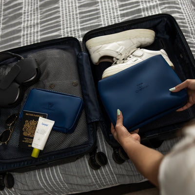 A female packing the Havelock Blue Wash Bag & Eco Essentials Pouch into a carry on suitcase, on a bed