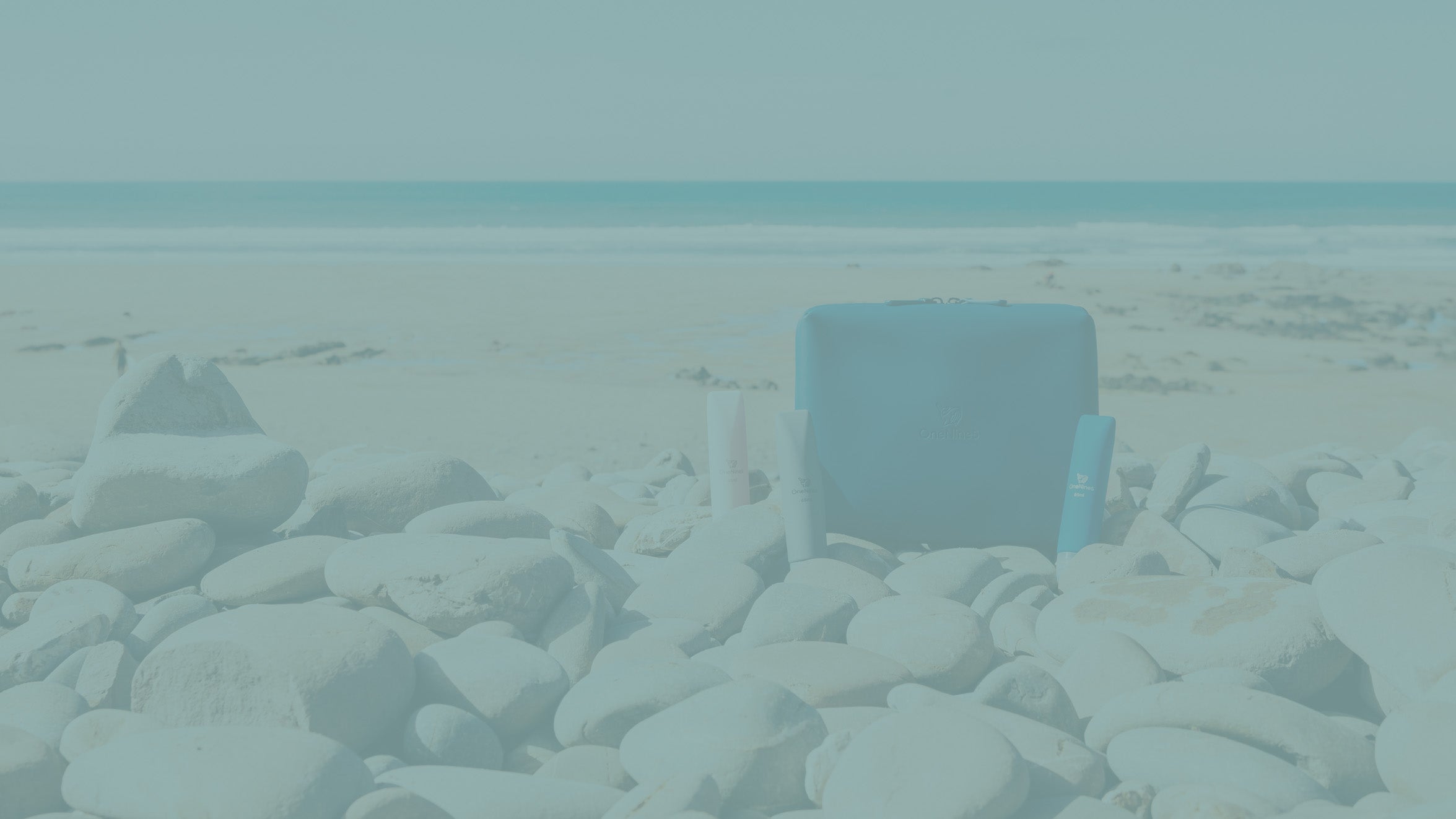 A banner image of the Havelock Blue Eco-Conscious Wash Bag & refillable silicone bottles on a beach