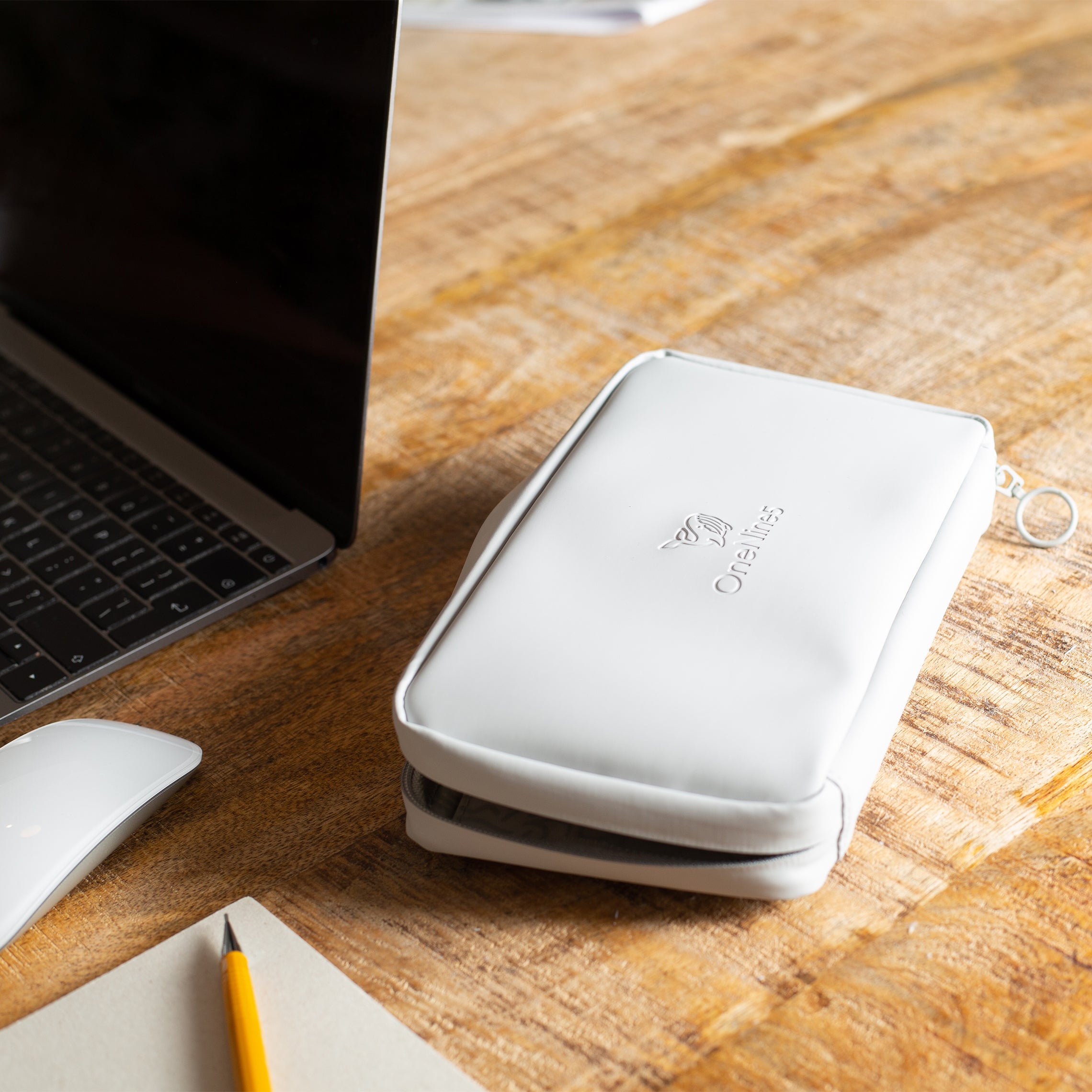 The Moeraki Grey Eco Essentials Pouch is zipped open and laid flat on a brown wooden desk. To the left of the open pouch is an Apple Macbook, an Apple Mouse, a small notepad and a yellow pencil